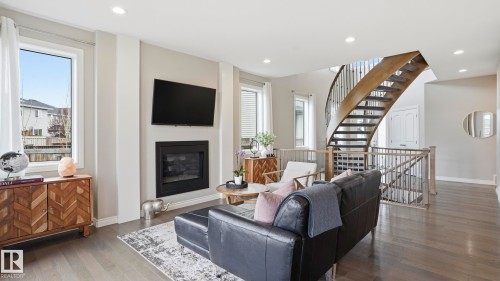 Open concept living space featuring a curved wood staircase with wrought iron spindles, a sleek black fireplace surround, and recessed lighting - 2620 Adam Crest, Edmonton, AB - Indoor Photo Showing Living Room With Fireplace