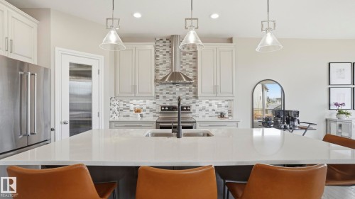 Kitchen featuring an expansive center island with seating, a stainless steel refrigerator, white shaker-style cabinetry, a tile backsplash, and stainless steel appliances - 2620 Adam Crest, Edmonton, AB - Indoor Photo Showing Kitchen With Stainless Steel Kitchen With Upgraded Kitchen