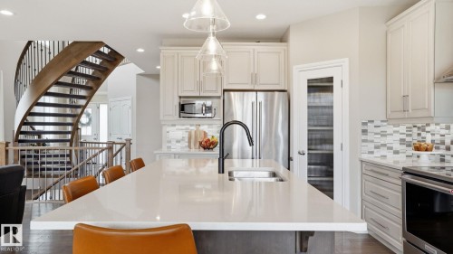Open-concept kitchen featuring a spacious island with an integrated sink, light-toned cabinetry, stainless steel appliances, and a geometric tile backsplash - 2620 Adam Crest, Edmonton, AB - Indoor Photo Showing Kitchen With Double Sink With Upgraded Kitchen