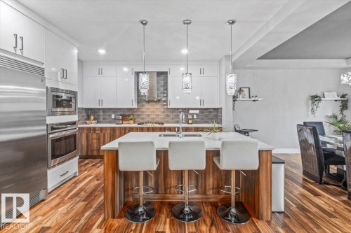 Modern kitchen featuring white cabinetry, stainless steel appliances, a center island with seating, a tile backsplash, and wood-finish flooring - 219 Cranberry Bend, Fort Saskatchewan, AB - Indoor Photo Showing Other Room