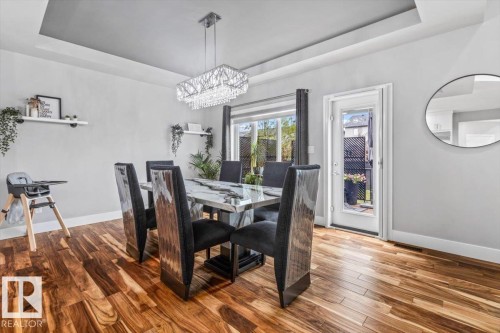 Dining area featuring wood-finish flooring, a tray ceiling, and a contemporary crystal chandelier - 219 Cranberry Bend, Fort Saskatchewan, AB - Indoor Photo Showing Dining Room