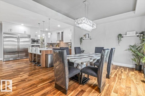 Open-concept dining area featuring wood-finish flooring, a contemporary chandelier, and a tray ceiling detail - 219 Cranberry Bend, Fort Saskatchewan, AB - Indoor Photo Showing Dining Room