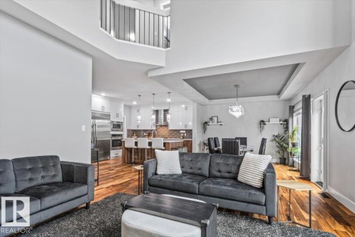 Spacious open-concept living area featuring high ceilings, wood-finish flooring, a contemporary chandelier, recessed lighting, and a kitchen with stainless steel appliances - 219 Cranberry Bend, Fort Saskatchewan, AB - Indoor Photo Showing Living Room