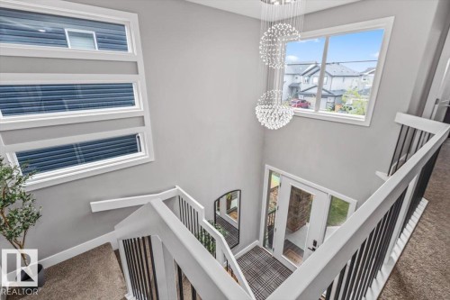 Entryway featuring a double-pane glass door, two statement crystal chandeliers, a large picture window, and a modern stair railing with black balusters - 219 Cranberry Bend, Fort Saskatchewan, AB - Indoor Photo Showing Other Room