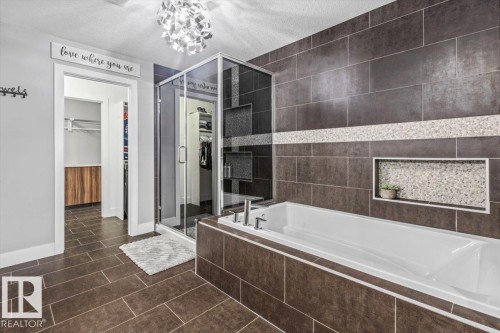Bathroom featuring dark tile flooring, a built-in soaking tub with dark tile surround, and a glass-enclosed shower with contrasting wall tile - 219 Cranberry Bend, Fort Saskatchewan, AB - Indoor Photo Showing Bathroom