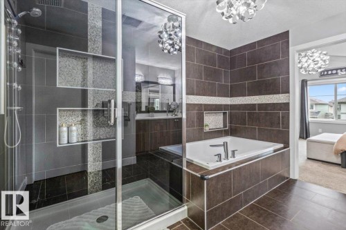 Contemporary bathroom featuring a spacious glass-enclosed shower with multiple built-in niches, a large soaking tub, and stylish tile flooring - 219 Cranberry Bend, Fort Saskatchewan, AB - Indoor Photo Showing Bathroom