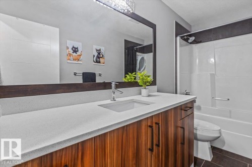 Bathroom vanity featuring a light-toned countertop with an integrated sink, dark wood-finish cabinetry, and contemporary dark hardware - 219 Cranberry Bend, Fort Saskatchewan, AB - Indoor Photo Showing Bathroom