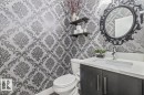 Powder room featuring ornamental wallpaper, a dark wood-finish vanity with a light countertop, an integrated sink basin, and a decorative black-framed mirror - 219 Cranberry Bend, Fort Saskatchewan, AB  - Indoor Photo Showing Bathroom 
