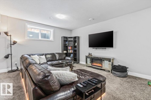 Carpeted room with a wall-mounted television, an electric fireplace with a mirrored surround, a built-in corner bookshelf, and a horizontal window - 219 Cranberry Bend, Fort Saskatchewan, AB - Indoor Photo Showing Living Room With Fireplace