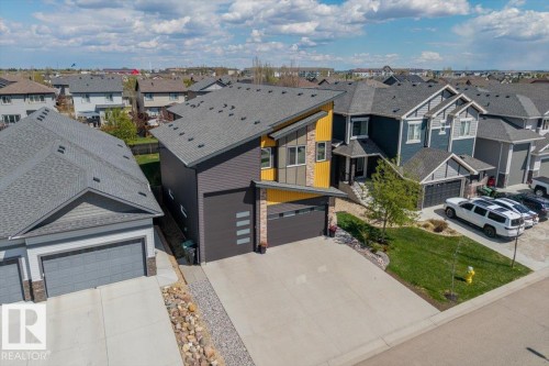 Modern architectural residence featuring a prominent slanted roofline, a two-car attached garage with horizontal frosted glass accents, and a contrasting facade of dark siding with bright yellow and gray paneling - 219 Cranberry Bend, Fort Saskatchewan, AB - Outdoor