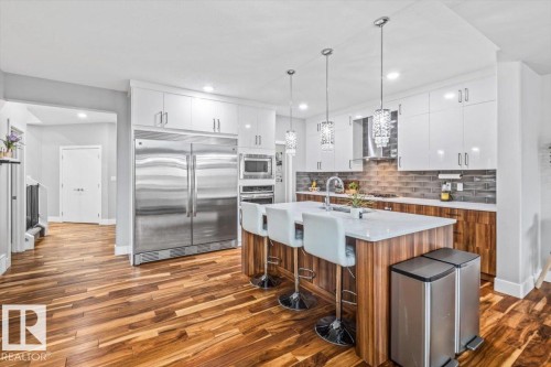 Modern kitchen featuring wood-finish flooring, white flat-panel cabinetry, stainless steel appliances, a center island with seating, and decorative pendant lighting - 219 Cranberry Bend, Fort Saskatchewan, AB - Indoor Photo Showing Kitchen With Stainless Steel Kitchen With Upgraded Kitchen