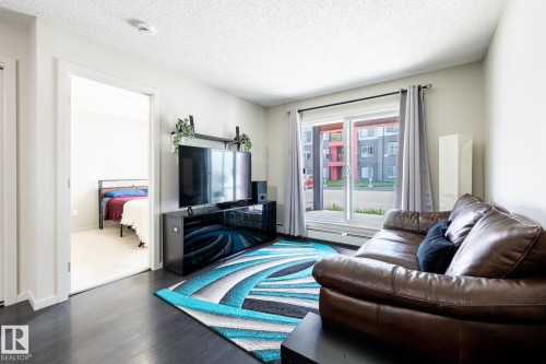 Living area featuring dark wood-finish flooring, light-toned walls, and a sliding glass door - 131 344 Windermere Road, Edmonton, AB - Indoor Photo Showing Living Room