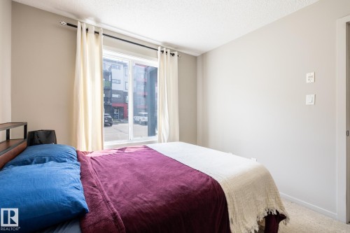 Bedroom featuring a large window, textured ceiling, light neutral wall paint, and soft carpet flooring - 131 344 Windermere Road, Edmonton, AB - Indoor Photo Showing Bedroom