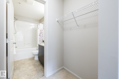 Bathroom featuring a tub/shower combination with white surround, a toilet, and a vanity with a dark gray base cabinet and light countertop - 131 344 Windermere Road, Edmonton, AB - Indoor