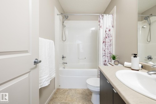 Bathroom featuring a white bathtub and shower combination, a single vanity with an integrated sink, a light-toned countertop, and dark wood-finish cabinetry - 131 344 Windermere Road, Edmonton, AB - Indoor Photo Showing Bathroom