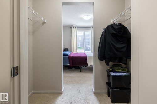 Hallway with beige carpeting and light-toned walls, featuring two recessed closet spaces with wire shelving - 131 344 Windermere Road, Edmonton, AB - Indoor With Storage