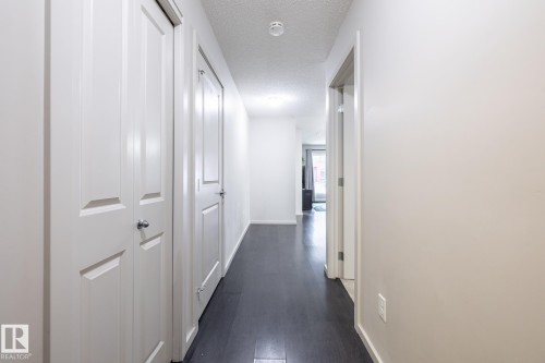 Entryway corridor featuring dark wood-finish flooring, light-colored walls, and white paneled doors - 131 344 Windermere Road, Edmonton, AB - Indoor Photo Showing Other Room