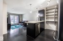 Open-concept living space featuring dark wood-finish flooring, a kitchen island with a light-toned countertop, stainless steel appliances, and built-in shelving - 131 344 Windermere Road, Edmonton, AB  - Indoor Photo Showing Kitchen With Upgraded Kitchen 