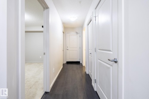 Hallway featuring dark wood-finish flooring, light-colored walls, and multiple panel doors - 131 344 Windermere Road, Edmonton, AB - Indoor Photo Showing Other Room