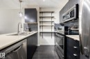 Modern kitchen featuring dark cabinetry, stainless steel appliances, light countertops, a double basin sink with a gooseneck faucet, and open shelving - 131 344 Windermere Road, Edmonton, AB  - Indoor Photo Showing Kitchen With Double Sink 