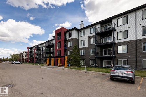 Contemporary multi-story building featuring a facade of light and dark horizontal siding, red architectural accents, multiple private balconies, and a paved parking area - 131 344 Windermere Road, Edmonton, AB - Outdoor With Facade