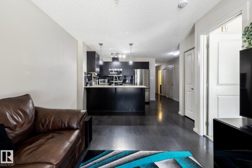 Open-concept living space featuring dark wood-finish flooring, a kitchen island with pendant lighting, dark cabinetry, and stainless steel appliances - 131 344 Windermere Road, Edmonton, AB - Indoor