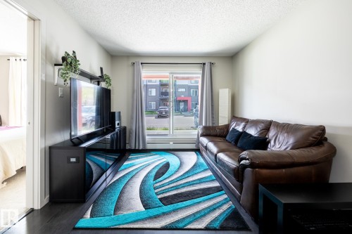Dark wood-finish flooring complements light-toned walls - 131 344 Windermere Road, Edmonton, AB - Indoor Photo Showing Living Room