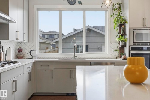Modern kitchen featuring light gray cabinetry with brushed nickel hardware, white stone-finish countertops, and a full-height herringbone tile backsplash - 2116 159 Street, Edmonton, AB - Indoor Photo Showing Kitchen With Upgraded Kitchen