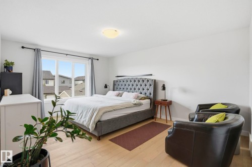 Light wood-finish flooring provides a bright base for this room featuring a large window with white trim, a flush-mount ceiling light fixture, and white walls - 2116 159 Street, Edmonton, AB - Indoor Photo Showing Bedroom