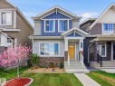 Two-story home with a blue and light gray exterior, stone facade accents, a bright yellow front door, white porch pillars, and a mature flowering tree in the front yard - 2116 159 Street, Edmonton, AB  - Outdoor With Facade 