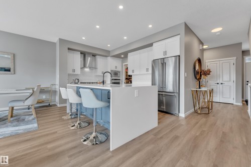 The property features a modern kitchen with light wood-tone flooring, white cabinetry, and a blue island with a white countertop - 21853 98A Avenue, Edmonton, AB - Indoor Photo Showing Kitchen With Upgraded Kitchen