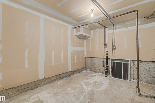 Unfinished interior space featuring exposed drywall with taped seams, a concrete floor, and visible plumbing and electrical conduits - 5953 40 Avenue, Edmonton, AB - Indoor