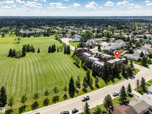 Multi-story building featuring brick and dark-colored siding, surrounded by mature evergreen trees - 5953 40 Avenue, Edmonton, AB 