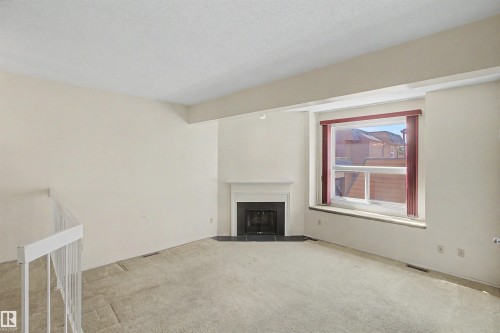 Living area featuring a white fireplace mantel with a black stone surround and hearth, a large window with vertical blinds, and a white railing - 5953 40 Avenue, Edmonton, AB - Indoor With Fireplace