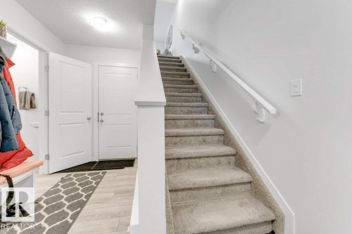 Entryway featuring light wood-finish flooring, a carpeted staircase with a white handrail, and two white panel doors - 53 1110 Daniels Link Link, Edmonton, AB - Indoor Photo Showing Other Room