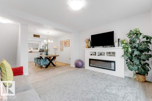 Spacious living area featuring light wood-finish flooring and a built-in entertainment unit with an electric fireplace - 53 1110 Daniels Link Link, Edmonton, AB - Indoor