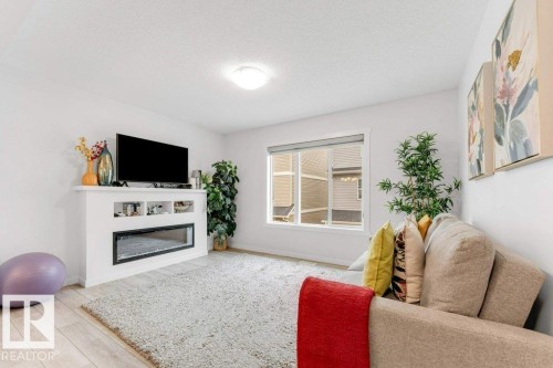 Living area featuring a built-in electric fireplace with display shelving, a large window, light wood-finish flooring, and a flush-mount ceiling light - 53 1110 Daniels Link Link, Edmonton, AB - Indoor Photo Showing Living Room