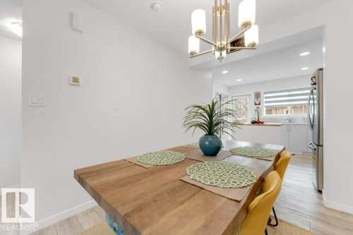 Open-concept dining area featuring a contemporary chandelier, wood-finish flooring, and a pass-through to the kitchen - 53 1110 Daniels Link Link, Edmonton, AB - Indoor Photo Showing Other Room