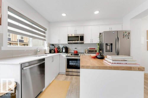 Modern kitchen featuring white cabinetry, stainless steel appliances, a center island with a wood-finish countertop, white quartz countertops, and light wood-finish flooring - 53 1110 Daniels Link Link, Edmonton, AB - Indoor Photo Showing Kitchen With Stainless Steel Kitchen