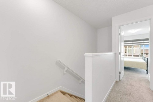 Carpeted staircase with white handrail and half-wall railing, opening to a carpeted hallway - 53 1110 Daniels Link Link, Edmonton, AB - Indoor Photo Showing Other Room