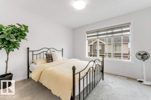Bright bedroom featuring a large window with dual-layer shades, neutral carpeting, and a flush-mount ceiling light fixture - 53 1110 Daniels Link Link, Edmonton, AB - Indoor Photo Showing Bedroom