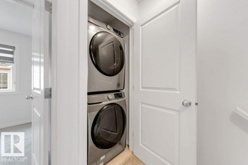 Dedicated laundry closet featuring a stacked washer and dryer unit with stainless steel finishes and a light-toned tile floor - 53 1110 Daniels Link Link, Edmonton, AB - Indoor Photo Showing Laundry Room
