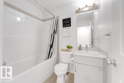 Bathroom featuring a white bathtub with a shower, a vanity with an integrated sink, a mirror, and wood-finish flooring - 53 1110 Daniels Link Link, Edmonton, AB - Indoor Photo Showing Bathroom