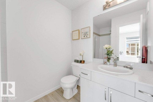 Bright bathroom featuring a single vanity with an integrated sink, a large mirror, a white toilet, and wood-finish flooring - 53 1110 Daniels Link Link, Edmonton, AB - Indoor Photo Showing Bathroom