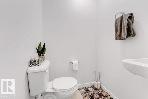 White-walled half bath featuring a white toilet, toilet paper holder, and a wall-mounted sink with a towel ring - 53 1110 Daniels Link Link, Edmonton, AB - Indoor Photo Showing Bathroom