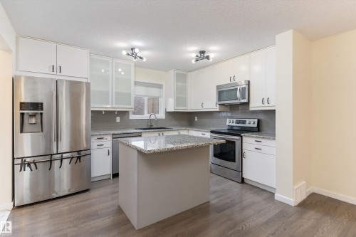 Kitchen featuring wood-finish flooring, white cabinetry, a central island, stainless steel appliances, and a gray tile backsplash - 336 Watt Boulevard, Edmonton, AB - Indoor Photo Showing Kitchen With Upgraded Kitchen
