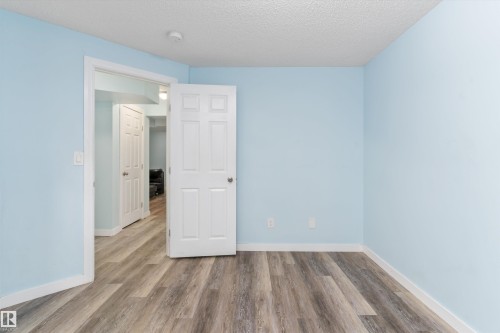 Spacious room featuring wood-finish flooring, light blue walls, white trim, and a six-panel door - 336 Watt Boulevard, Edmonton, AB - Indoor Photo Showing Other Room