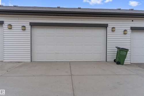 Garage exterior featuring a white paneled door, horizontal siding, dark fascia, and wall-mounted outdoor lighting fixtures - 336 Watt Boulevard, Edmonton, AB - Outdoor With Exterior