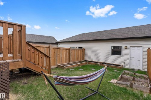 Private backyard space featuring a wooden deck with railing and stairs, full wooden privacy fencing, raised garden beds, and a white exterior wall with a door and window - 336 Watt Boulevard, Edmonton, AB - Outdoor