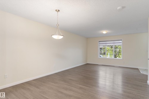 Expansive room featuring wood-finish flooring, neutral wall tones, a large window with a roller shade, and a brushed nickel pendant light fixture - 336 Watt Boulevard, Edmonton, AB - Indoor